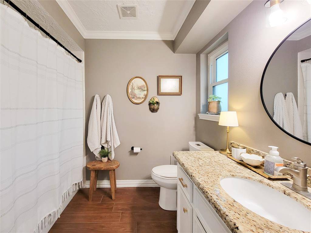 It includes a shower with a curtain, wood-look tile flooring, and tasteful decor. Natural light comes through the window, creating a bright and welcoming atmosphere.