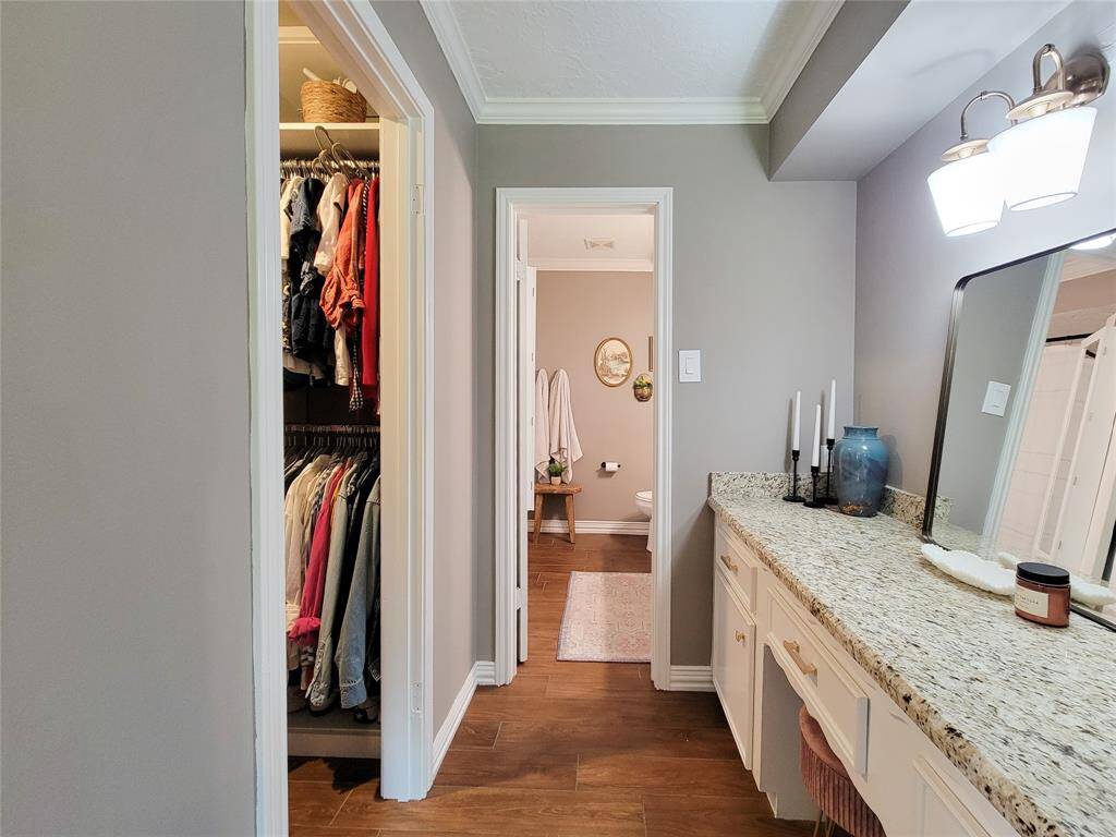 This photo features an adjacent walk-in closet with organized shelving and hanging space, opposite the vanity area.