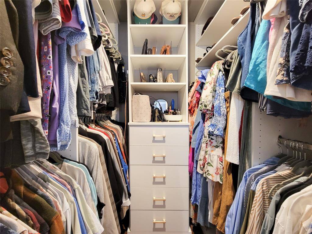 This photo showcases a well-organized walk-in closet with ample shelving and hanging space on both sides, featuring a central unit with drawers and open shelves for accessories and storage.
