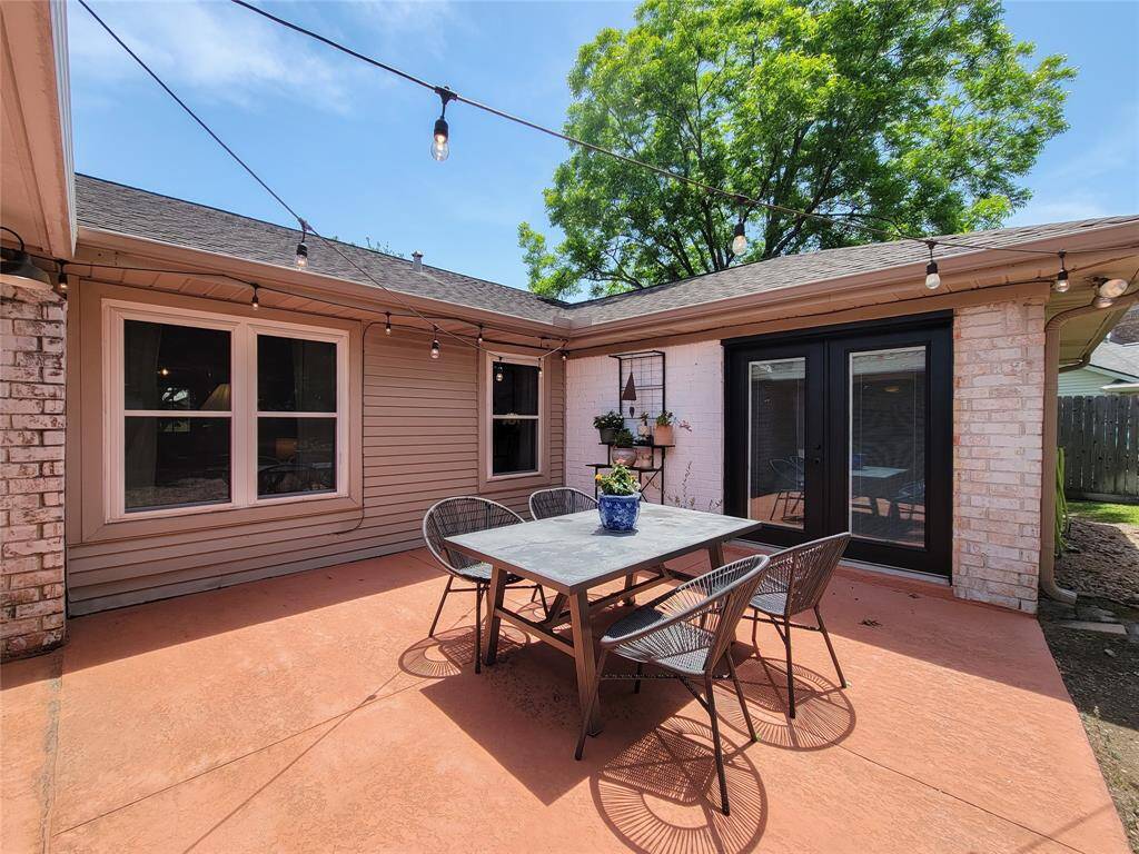 Charming outdoor patio featuring a modern dining set, string lights, and a mix of brick and siding exterior, with direct access from the primary bedroom through large glass doors and a view of a lush green tree.