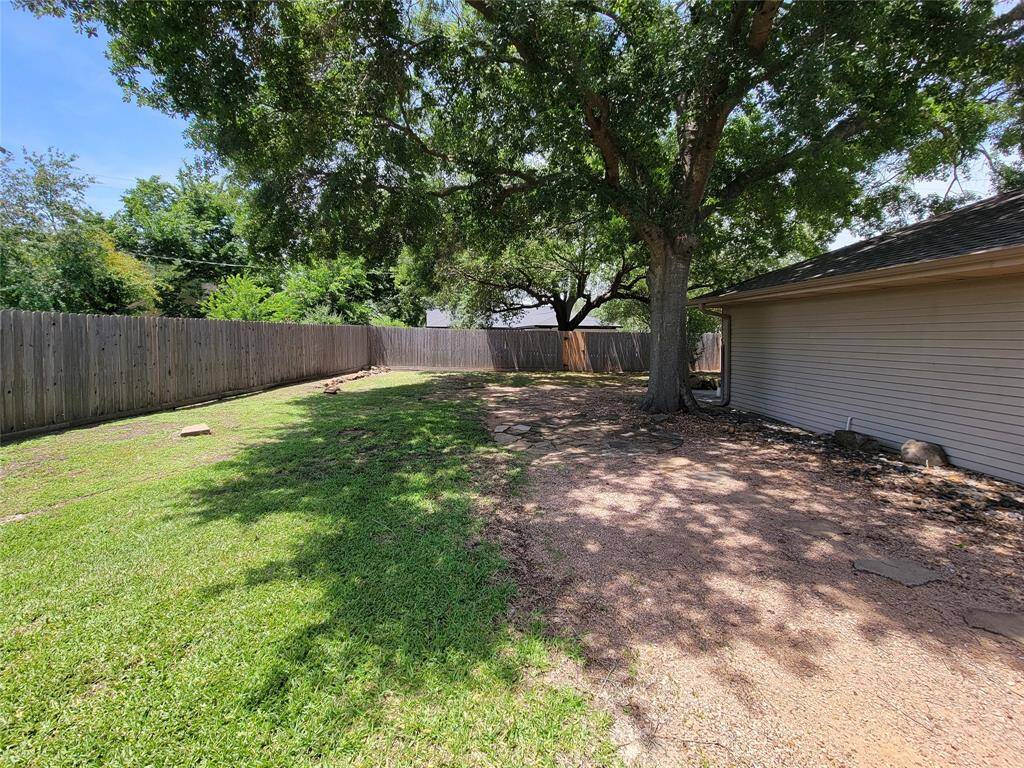 Spacious backyard with mature trees providing ample shade, a well-maintained lawn, and a wooden privacy fence. Ideal for outdoor activities and relaxation.