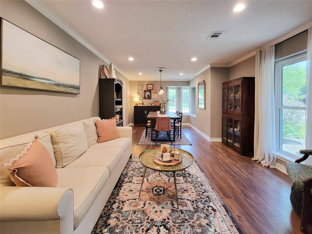This inviting living-dining area features warm Laminate flooring, neutral walls, and ample natural light from large windows. It includes a cozy sofa, elegant dining set, and tasteful decor, creating a welcoming atmosphere ideal for entertaining or relaxing.