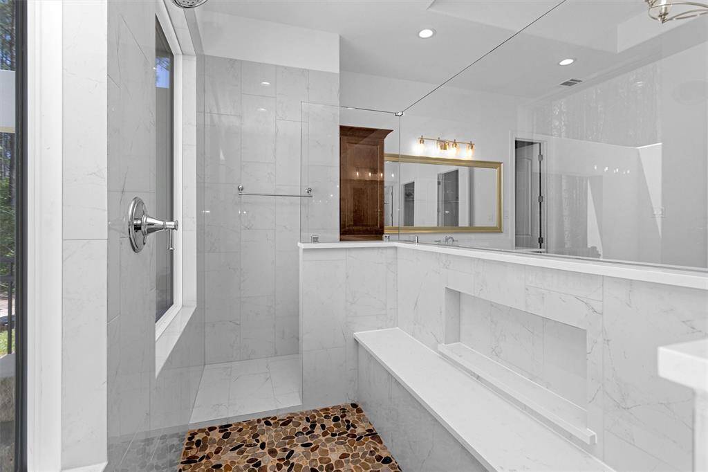 The oversized walk-in shower blends luxury and function with a river rock floor, tile surround, built-in bench, and spa-style fixtures—all bathed in natural light.