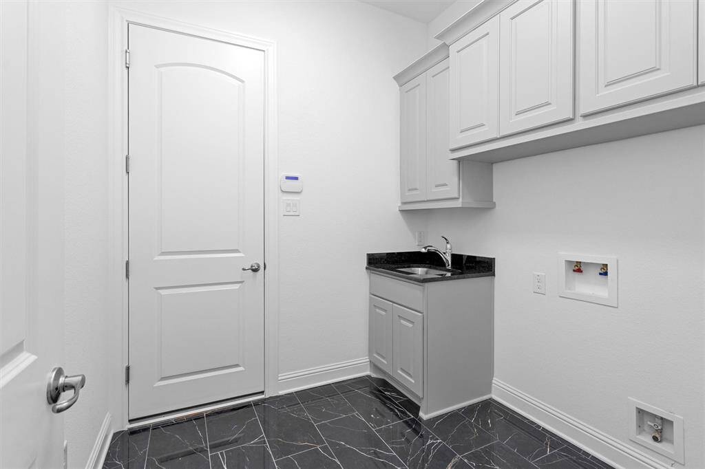 The laundry room is both functional and refined, offering upper cabinetry, a utility sink, and polished black granite counters atop striking marble tile floors.