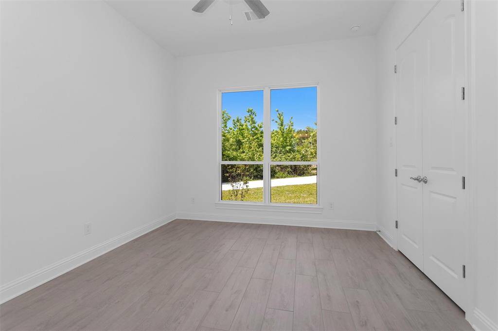 This light-filled secondary bedroom features wood-look tile flooring, a spacious closet, and peaceful views of the lush, tree-lined grounds.