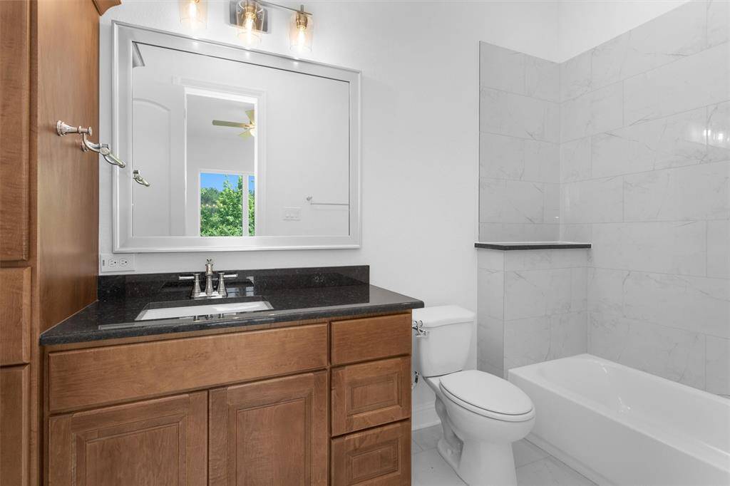 Secondary bedroom includes an en-suite bathroom featuring rich wood cabinetry, granite counters, and a sleek tub-shower combo wrapped in tile.
