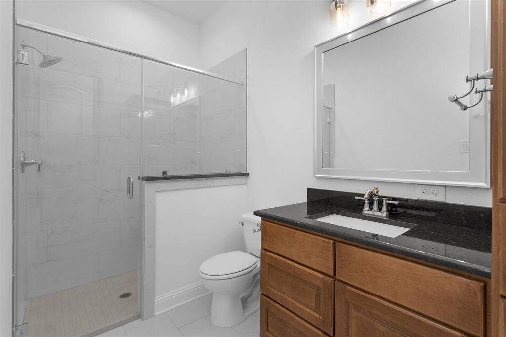 Another en-suite bathroom with a frameless glass walk-in shower, granite vanity, and warm wood cabinetry.