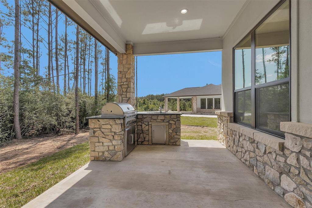 Surrounded by trees and set against a backdrop of both privacy and space, the covered outdoor kitchen is outfitted with a built-in grill, sink, stonework accents, and ample prep space for entertaining.