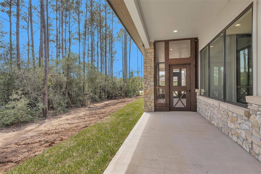 This peaceful covered patio offers a seamless connection to nature with wooded views, stone accents, and direct access to the screened porch and outdoor living spaces.