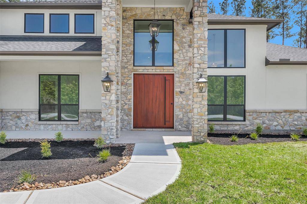 The grand entrance showcases a rich wooden door framed by a striking stone facade, tall windows, and elegant lantern lighting for a sophisticated welcome.