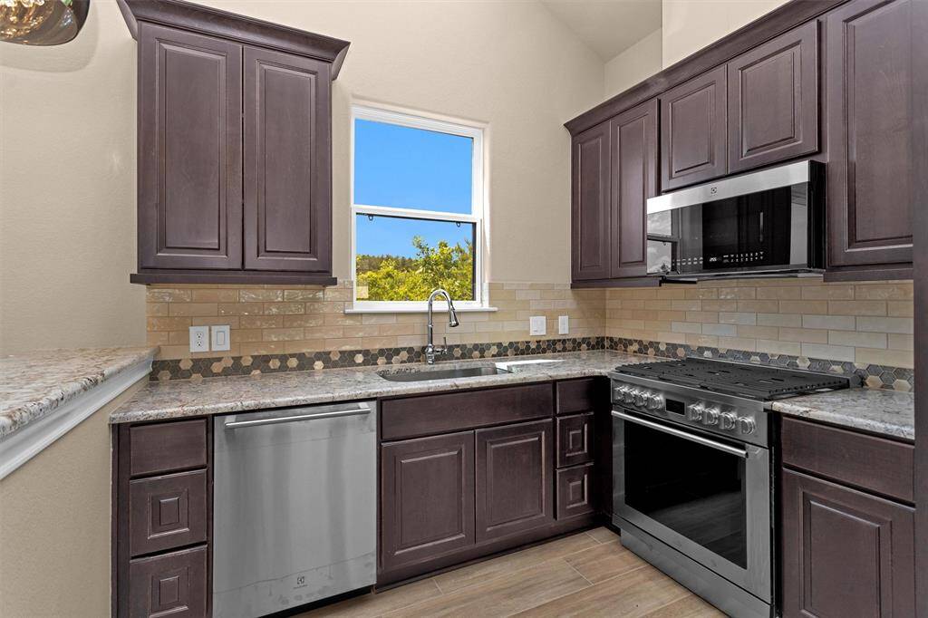 The guest home kitchen is beautifully appointed with rich cabinetry, granite countertops, a full suite of stainless appliances, and a scenic window above the sink.