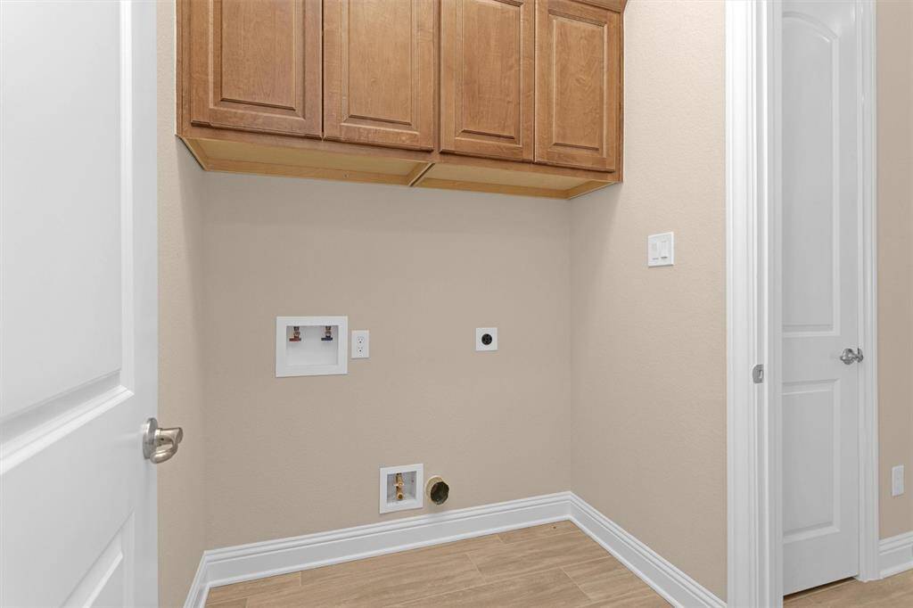 This laundry room offers upper cabinetry for extra storage, washer and dryer hookups, and easy-to-clean wood-look tile flooring in a clean, functional layout.