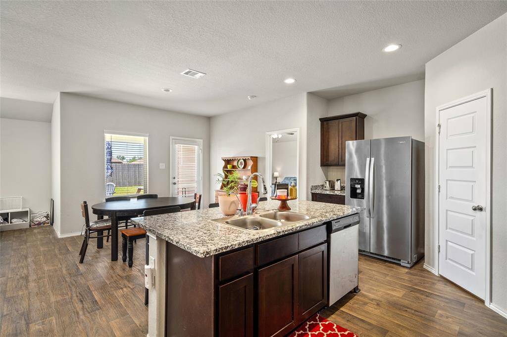This open-concept kitchen features a large granite-topped center island with dual sinks, perfect for meal prep and casual dining. Rich wood cabinetry offers ample storage, and the stainless steel appliances add a sleek, modern touch.