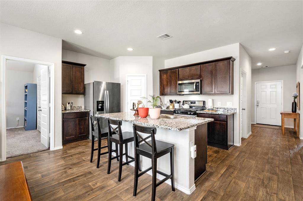 This side perspective showcases the kitchen's efficient layout and connection to surrounding spaces. The expansive island with bar seating serves as the heart of the home, while the adjoining pantry, stainless appliances, and ample counter space provide convenience for everyday cooking and entertaining.