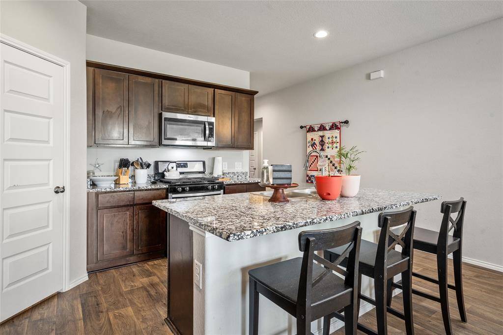 This modern kitchen boasts sleek granite countertops, rich cabinetry, and stainless steel appliances, all arranged in a smart, functional layout. The spacious island includes bar seating and overlooks the main living and entry areas, promoting a seamless flow for both daily living and entertaining.
