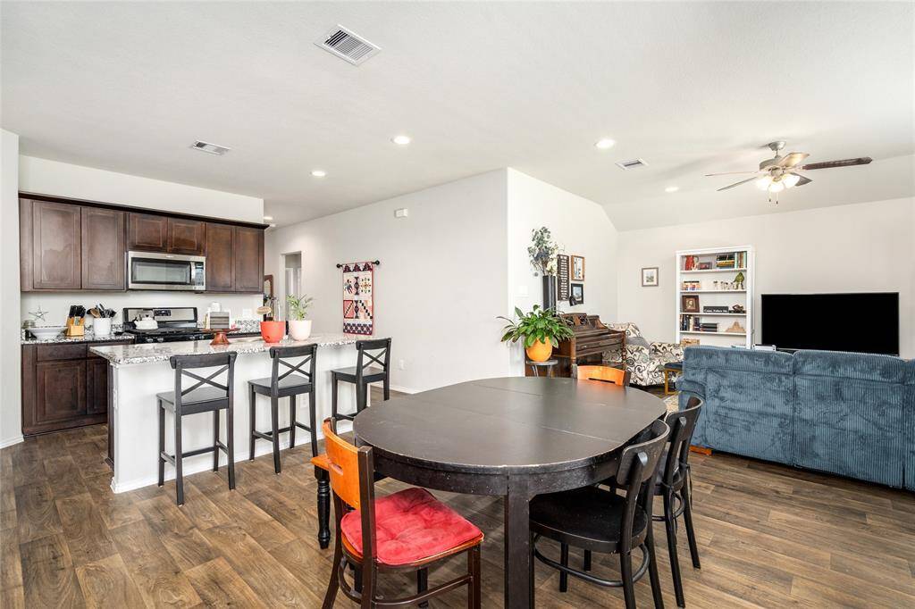 This wide-angle view captures the heart of the home—an open kitchen with a spacious island and bar seating that flows effortlessly into the dining and living areas. Perfect for hosting or everyday family living, the layout offers clear sightlines, cozy gathering spaces, and a welcoming atmosphere throughout.