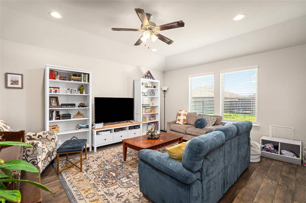 Enjoy natural light and comfort in this welcoming living room, highlighted by large windows, rich wood flooring, and recessed lighting. The space offers a cozy layout perfect for movie nights or quiet afternoons, complete with built-in shelving and room for personalized touches.