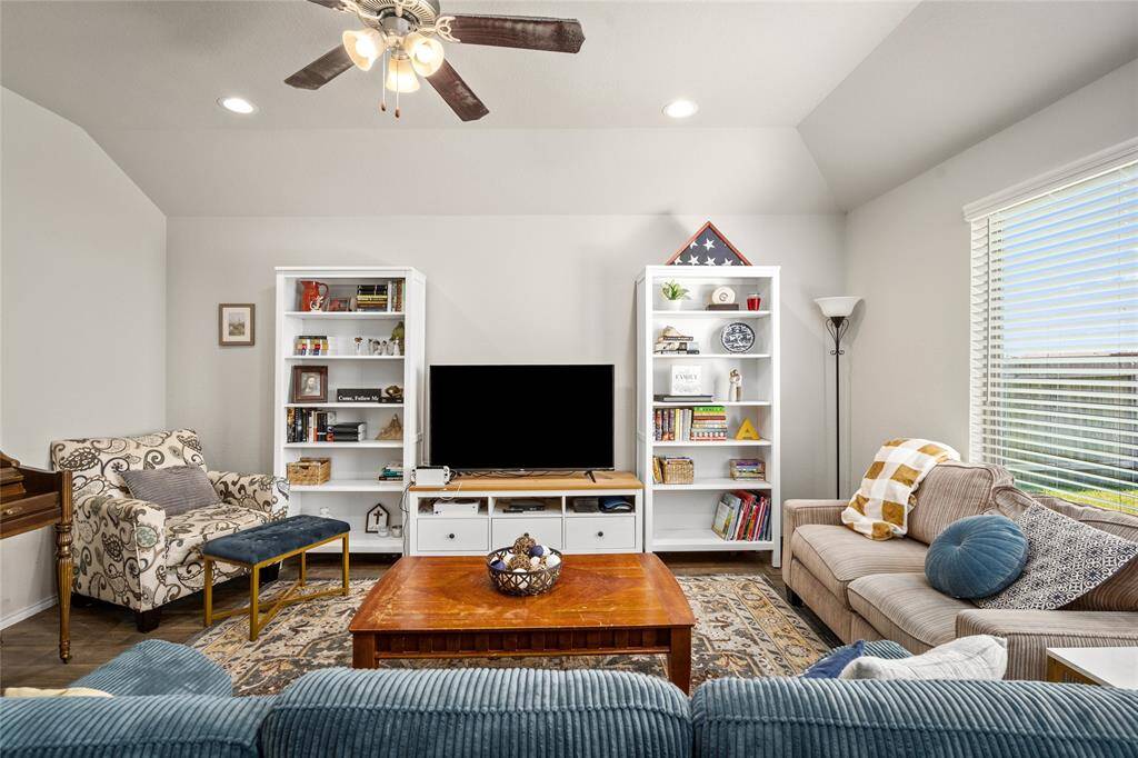 This spacious living area offers the perfect blend of comfort and style with its vaulted ceiling, recessed lighting, and modern ceiling fan. Large windows let in an abundance of natural light, illuminating the beautiful wood-look flooring and tasteful built-ins. Thoughtful furniture placement and a warm, neutral palette make this space ideal for relaxing or entertaining.