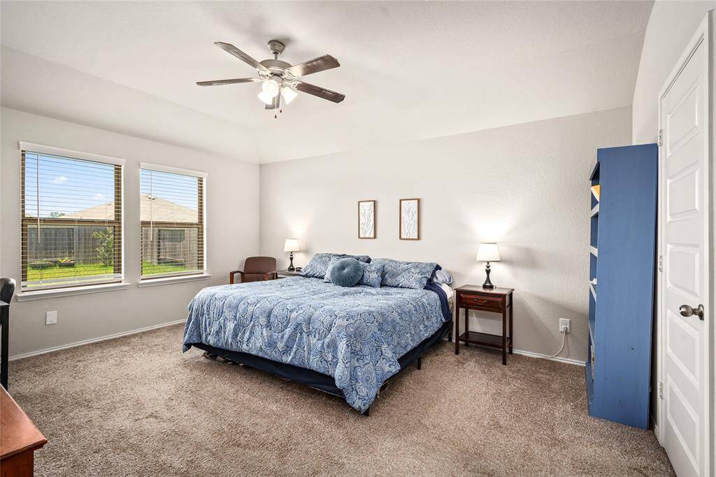 The primary bedroom offers a generous layout with ample room for a king-size bed and additional furnishings. Natural light pours in through three large windows overlooking the backyard, creating a bright and airy feel. A vaulted ceiling enhances the openness of the room, while plush carpeting adds comfort underfoot. Neutral wall tones provide a versatile backdrop, ready to complement any decor style. A standard ceiling fan offers added airflow and comfort year-round.