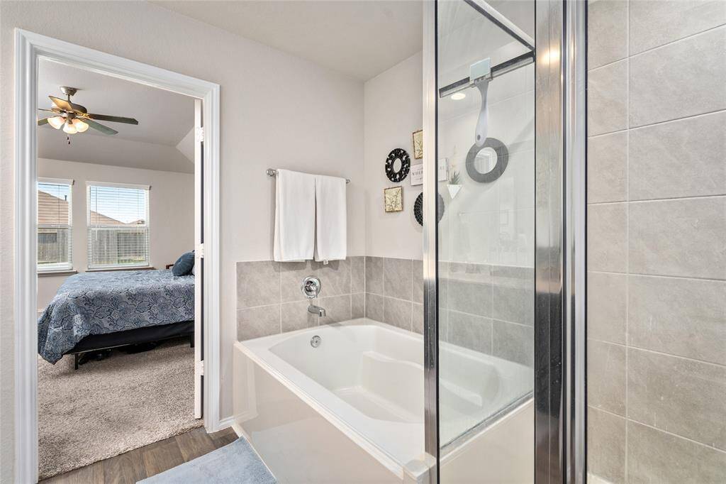 Unwind in the comfort of a deep soaking tub set against a modern tiled surround, creating a clean and calming retreat within the primary bath. Positioned beneath soft, neutral walls with tasteful accent decor, the tub offers a peaceful escape just steps from the bedroom. A nearby towel bar adds convenience, while the adjacent walk-in shower complements the space for a spa-like experience