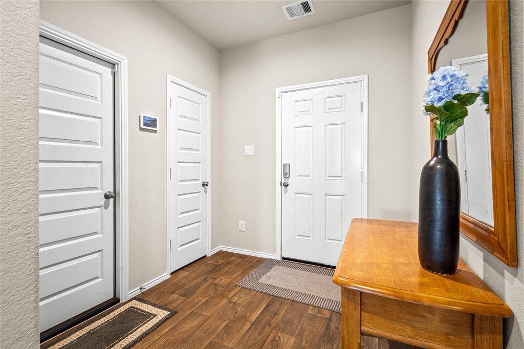Welcoming entryway with elegant wood-look flooring, neutral walls, and modern five-panel doors. A smart layout includes access to a coat closet, garage, and additional storage space. The space is accented by a decorative mirror and table, perfect for greeting guests with style.