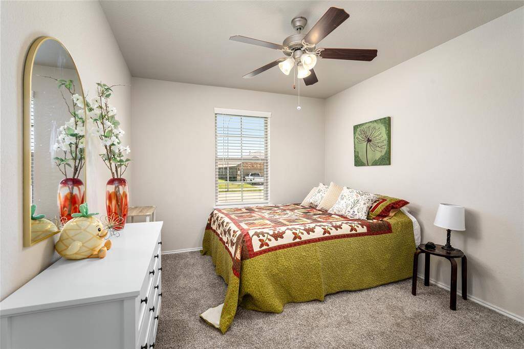 This cozy secondary bedroom features neutral walls and plush carpeting, creating a warm and inviting atmosphere. A large window allows for abundant natural light, enhancing the room’s bright and airy feel. The space is well-sized to accommodate a bed and additional furnishings, offering versatility for use as a guest room, home office, or personal retreat. A ceiling fan adds comfort and functionality.
