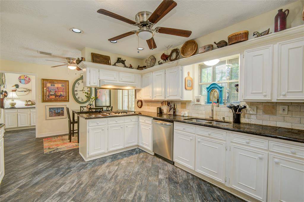 The spacious kitchen boasts stainless steel appliances, granite countertops, a gas cooktop, and wood-look tile flooring that seamlessly extends throughout the main living areas.