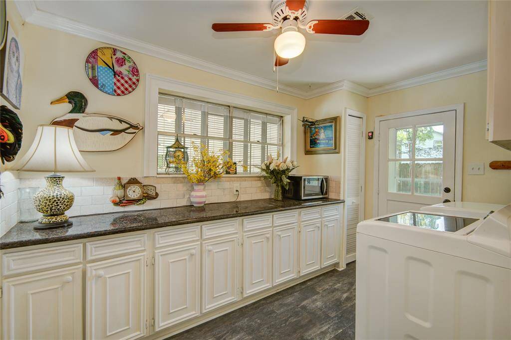 This view from inside the laundry room highlights crown molding, backyard-facing windows, upper cabinets over the included washer and dryer, and a convenient exit to the driveway.
