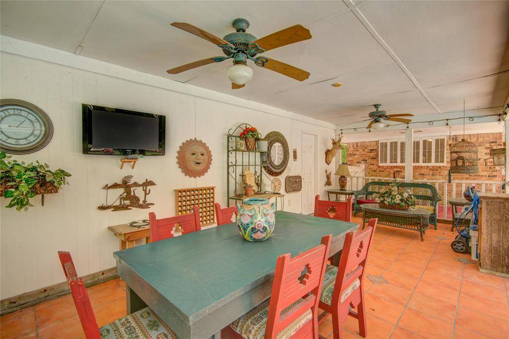 From beneath the covered patio, enjoy the cool breeze from overhead fans while relaxing on ample seating, with tiled flooring underfoot and a mounted TV for effortless entertainment.