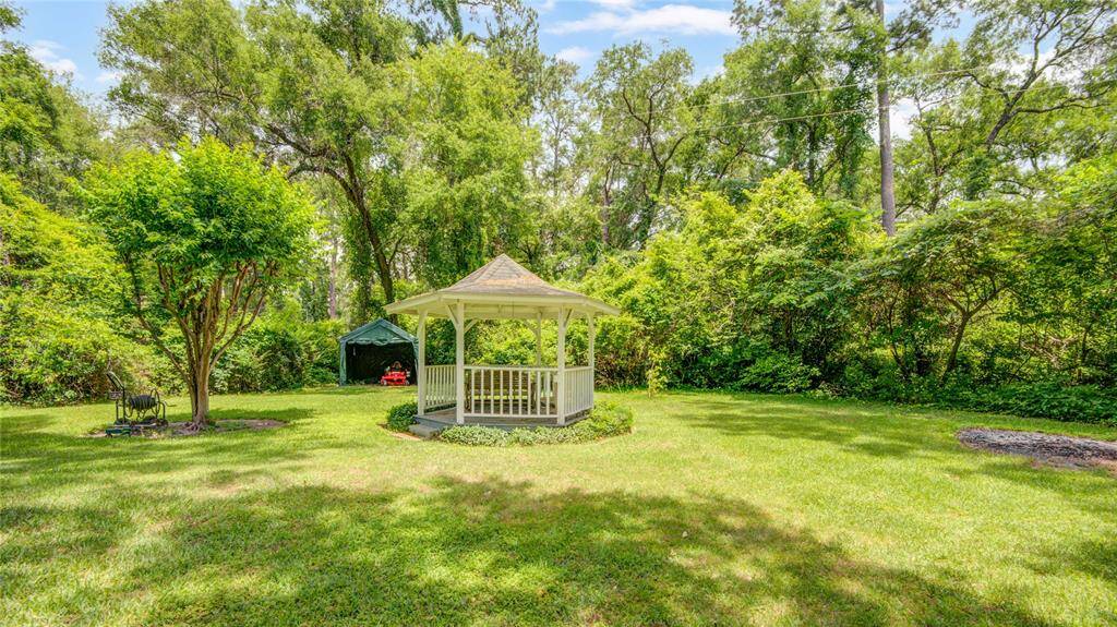The charming gazebo overlooks a practical storage area tucked beyond, where the riding mower is conveniently parked out of sight.