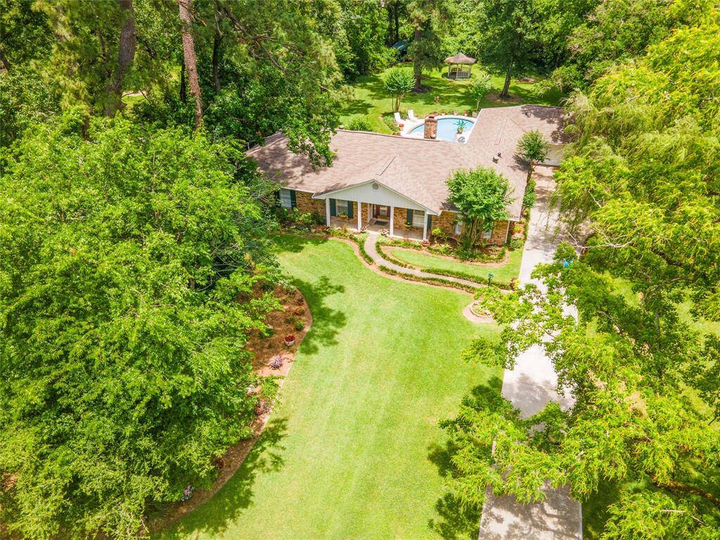 This aerial front view showcases the expansive, tree-filled lot with a glimpse of the backyard pool and gazebo nestled beyond the home.