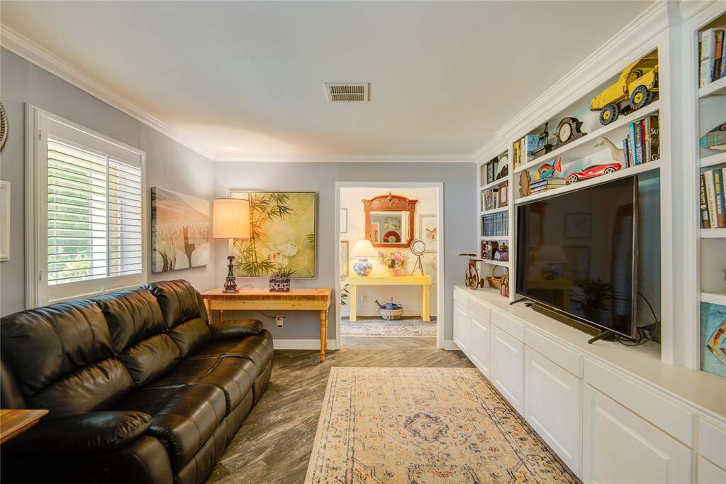 From the formal dining room, this view of the formal living room highlights a large plantation-shuttered window, a full wall of built-ins, and a clear line of sight into the foyer.