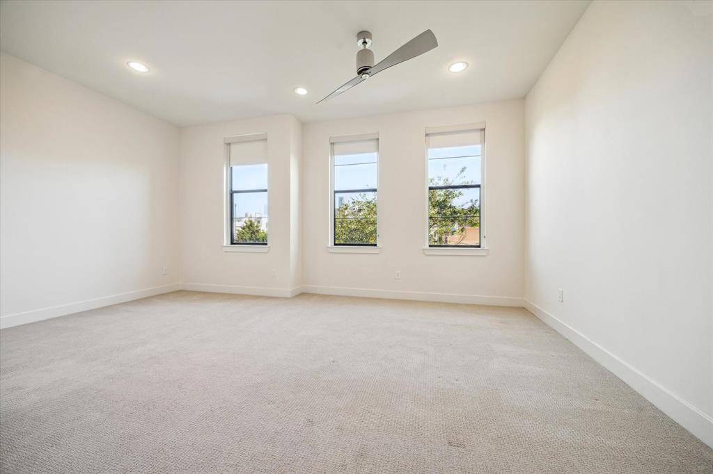 Another angle of the primary bedroom features three large windows for natural light creating a comfortable and airy atmosphere.  The black out shades can be drawn for a restful night.