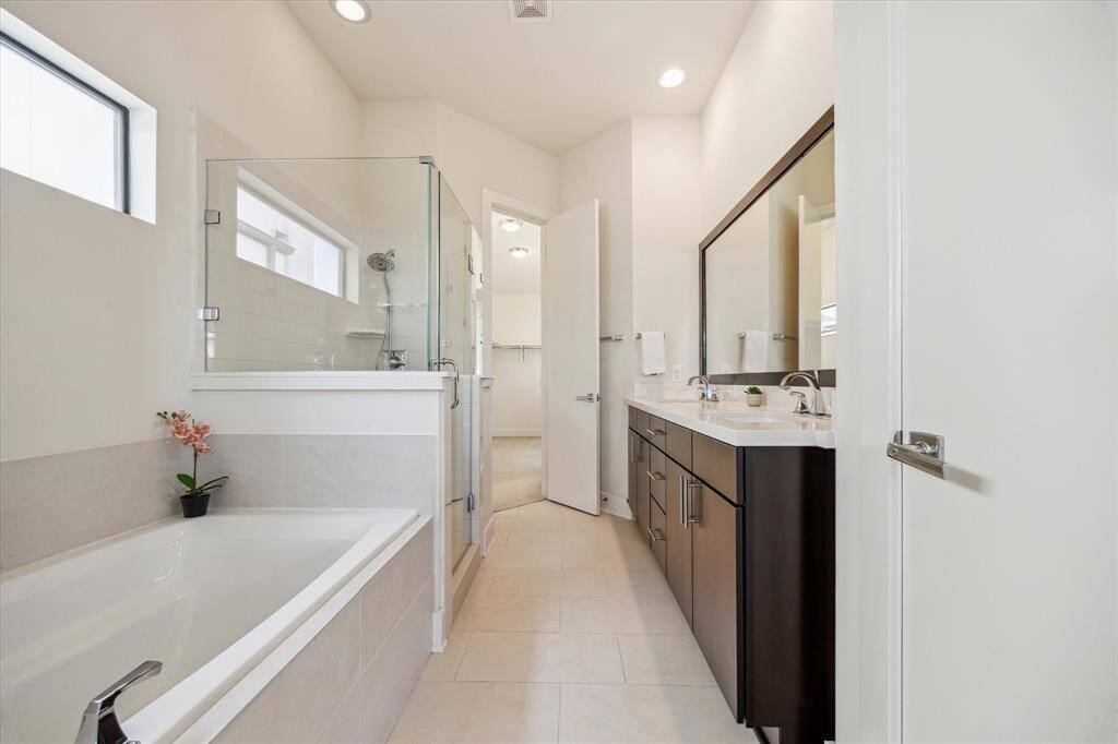 Clean and bright primary bathroom with glass-enclosed shower, a large bathtub, and a double-sink vanity.