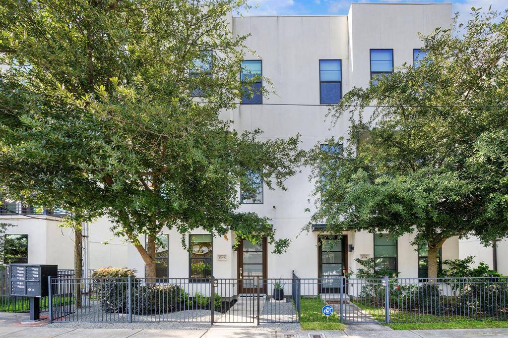 Modern white facade with glass door framed in wood, complemented by a stylish metal fence.