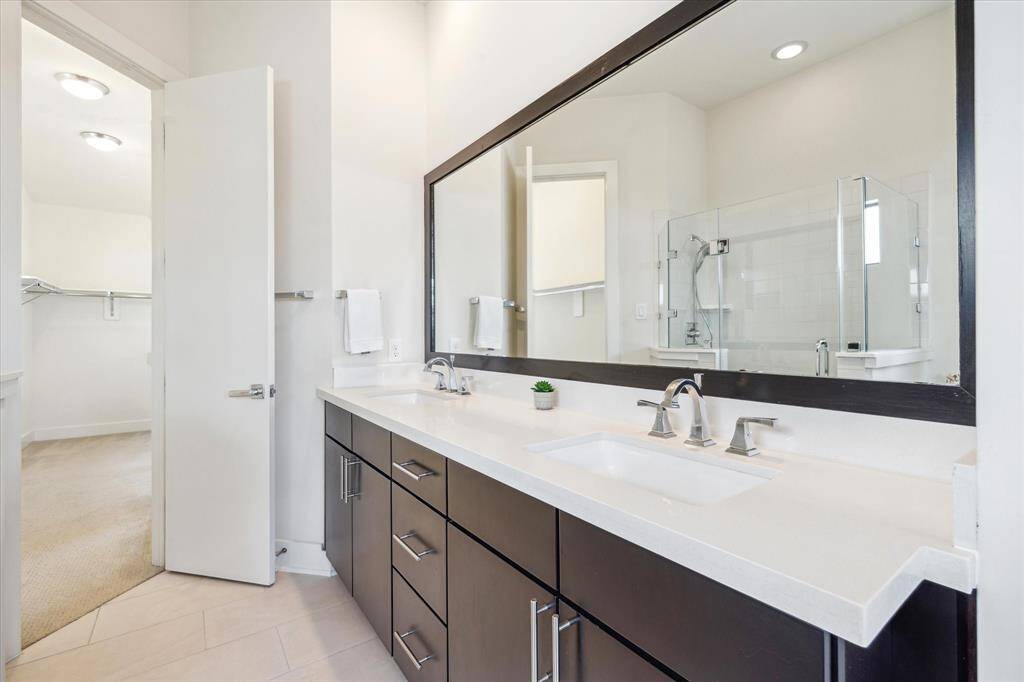 Dual sinks, elegant dark cabinetry, and a large mirror.  An adjoining walk-in closet is at the end of the bathroom.
