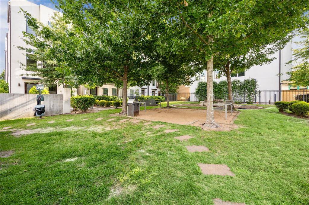 Well-maintained community park with lush green grass, mature trees providing shade, and a seating area. It's an inviting outdoor space ideal for relaxation and enjoying nature in the city.