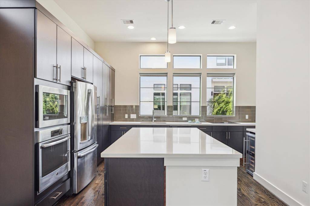 Stainless steel appliances, and a large island with a white quartz countertop. Ample natural light streams through multiple windows, highlighting the clean, contemporary design.