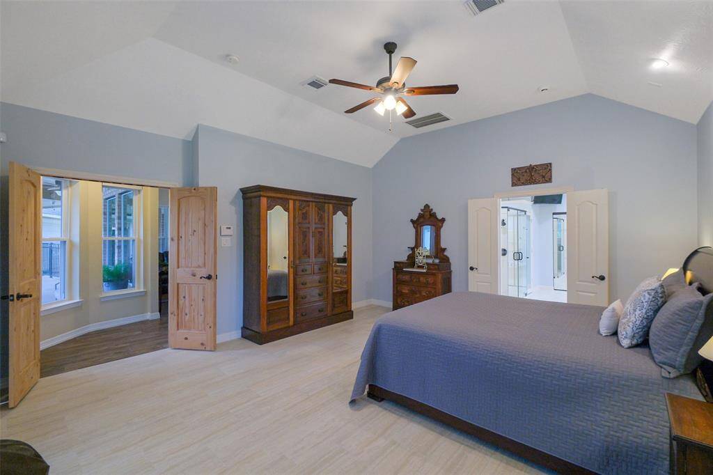The primary bedroom features vaulted ceilings, beautiful tile flooring, a ceiling fan, and ample natural light.
