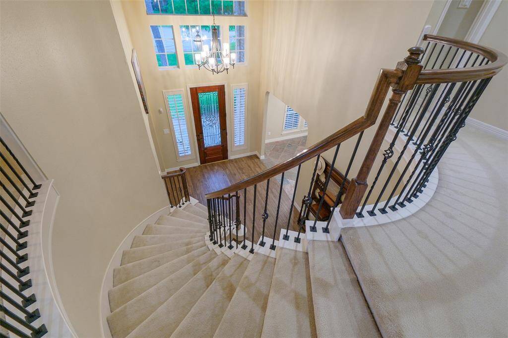 This photo showcases a grand, curved staircase with elegant iron balusters, leading down to a bright entryway featuring a tall wooden door flanked by large windows. The space is illuminated by a stylish chandelier, enhancing the open, airy feel.