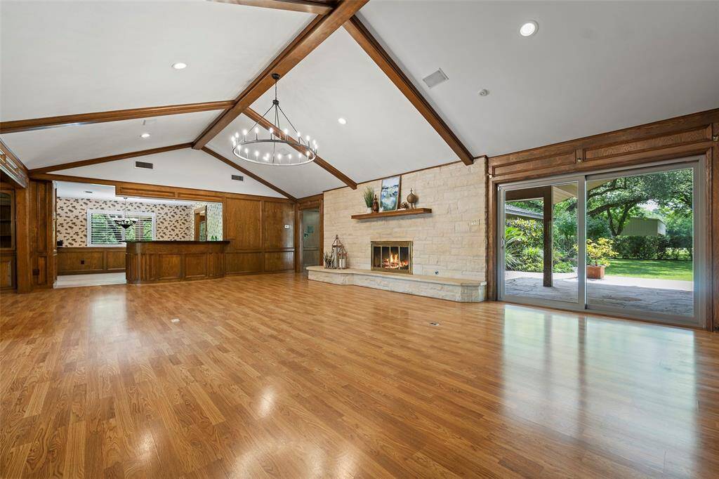 This spacious family room is a stunning blend of comfort and character, featuring soaring vaulted ceilings with exposed wood beams and rich wood paneling throughout. A grand stone fireplace serves as the centerpiece, offering a cozy focal point and inviting ambiance. The open layout boasts expansive wood-style flooring, built-in shelving—ideal for entertaining. Oversized sliding glass doors provide abundant natural light and seamless access to the covered patio and lush backyard!