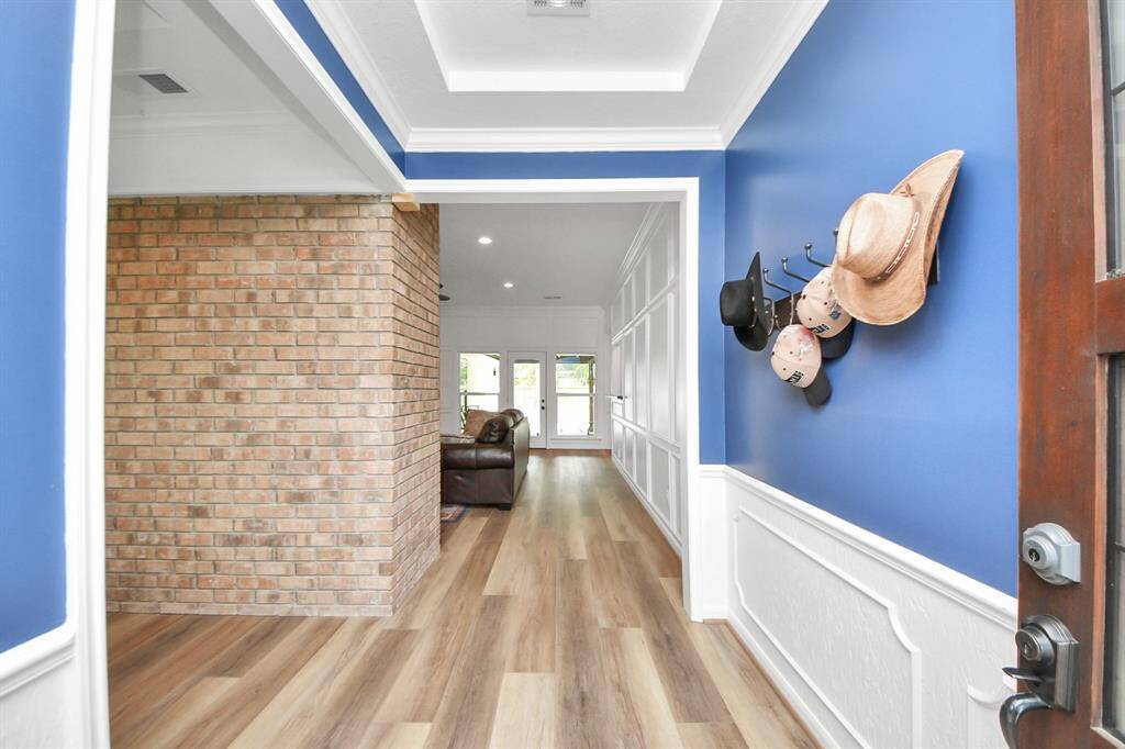 Step inside to a welcoming entry that sets the tone for this move-in ready home, featuring neutral engineered vinyl wood flooring, classic molding, a tiered ceiling, and a striking brick accent wall that adds warmth and character.
