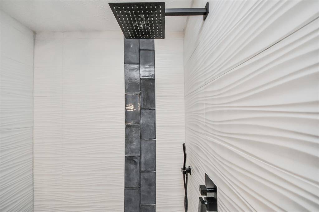 A closer look at the primary shower reveals exquisite tile work paired with a luxurious rain shower head, creating a serene and spa-like atmosphere.