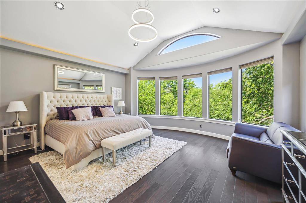 The primary suite, curved wall of windows allows for natural light and views of the lush treetops, high ceilings, engineered wood flooring and ample space for a sitting area.