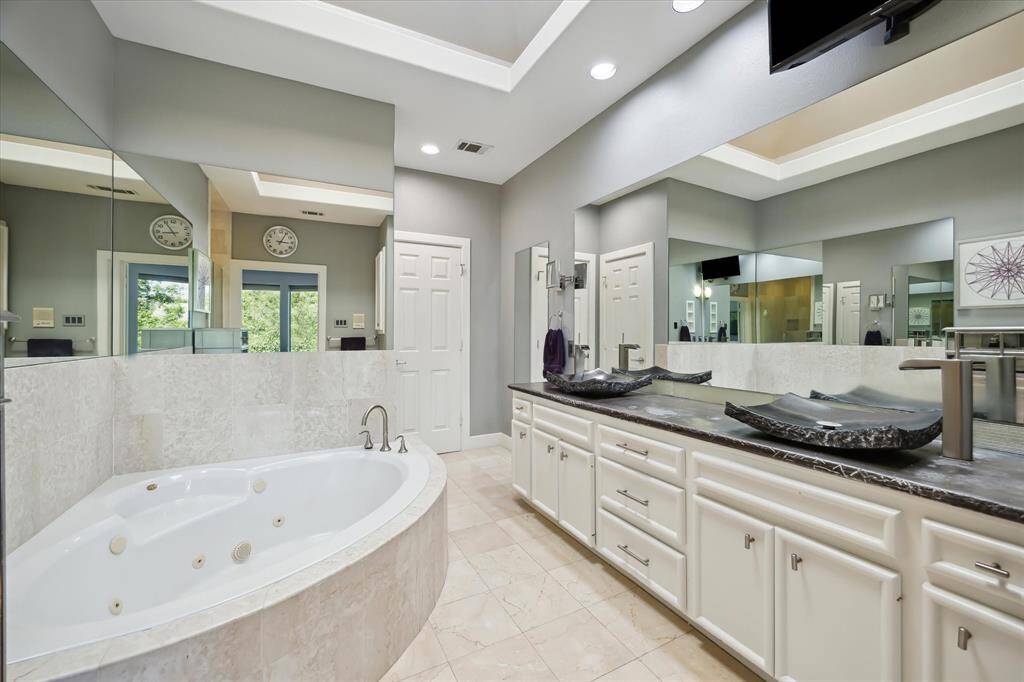 Secondary view of the jetted tub and dual vanity. Light fills the primary bath from the skylight.