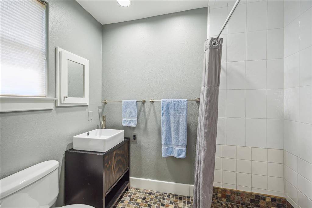 Third floor guest bathroom, single vanity, stone flooring is laid in a mosaic pattern and also on the shower floor.