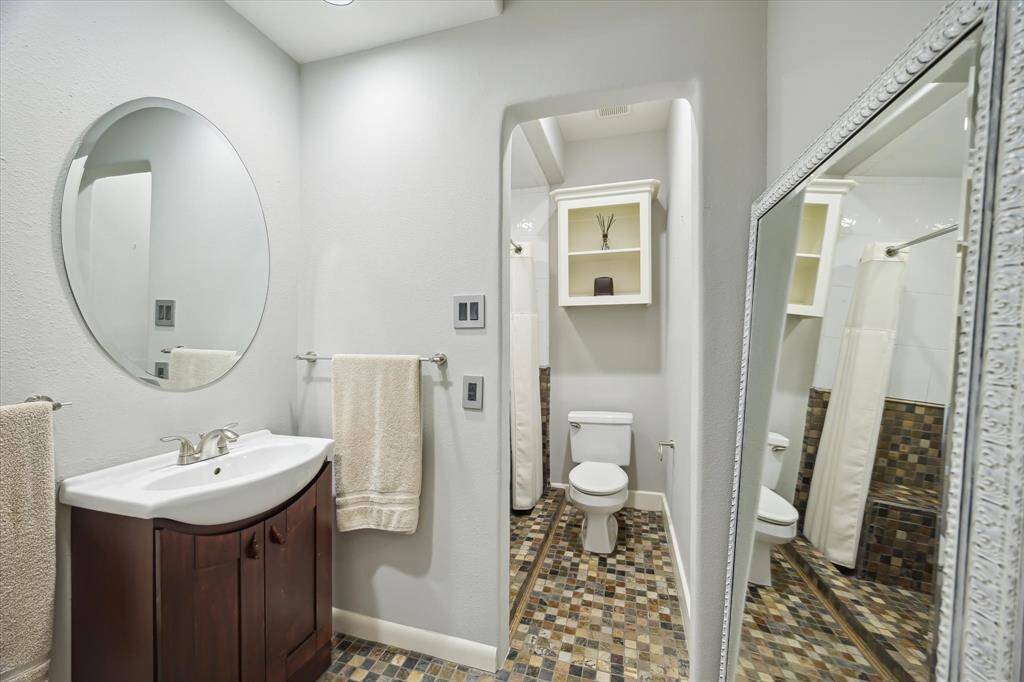 First guest ensuite bathroom, single vanity with storage, extra storage above the toilet, stone flooring is laid in a mosaic pattern and in the shower.