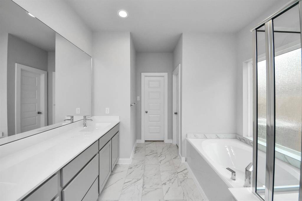Escape to a spa-like oasis in this primary bathroom. Enjoy a walk-in showerwith tile surround, a separate garden tub with custom detailing, and an elegantvanity featuring light countertops, modern hardware, and beautiful recessed lights.Experience luxury and relaxation in every detail.