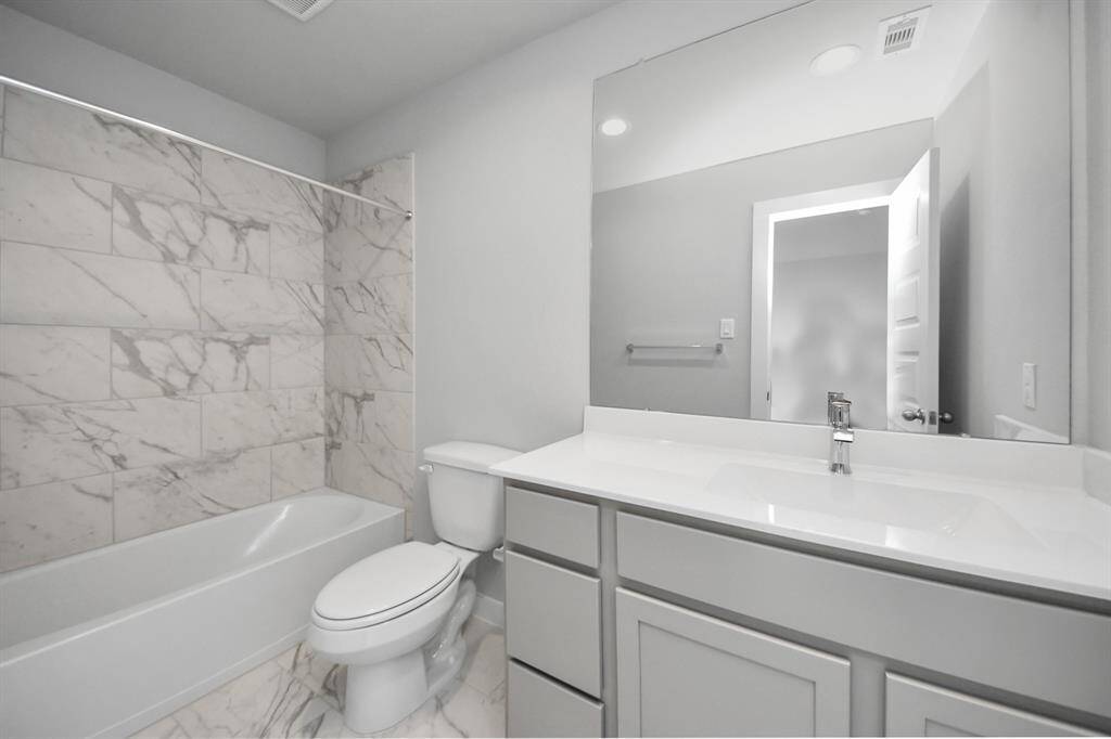 Secondary bath features tile flooring, bath/shower combo with tile surround, light stainedwood cabinets, beautiful light countertop.