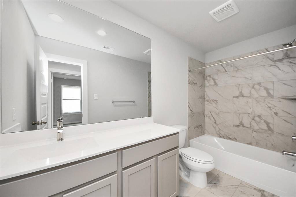 Secondary bath features tile flooring, bath/shower combo with tile surround, light stainedwood cabinets, beautiful light countertop.